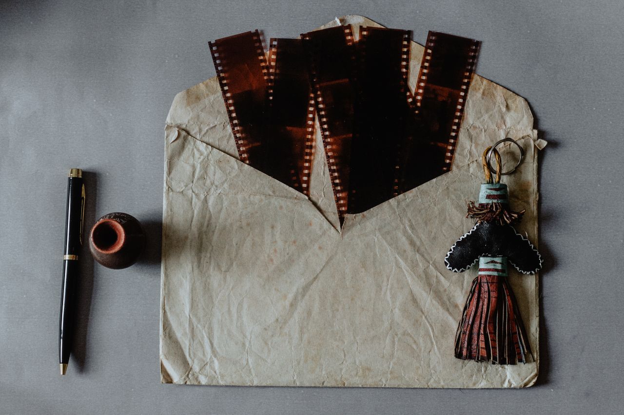 A rustic envelope holds vintage film negatives, a decorative figurine, and a pen on a textured surface.